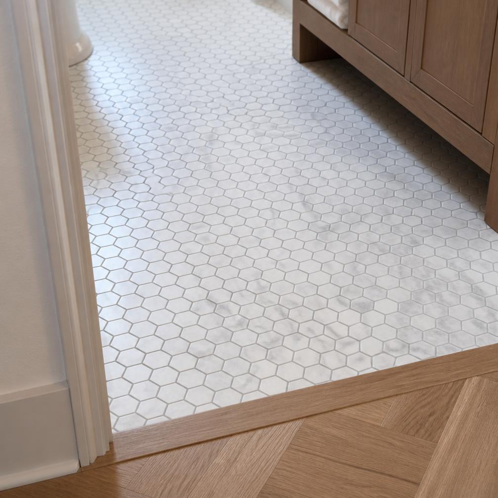 Marble hexagon mosaic floor tile meeting an oak threshold